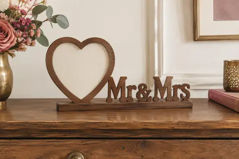 Petite décoration de mariage en bois brun associant un cadre photo en forme de cœur et les lettres Mr & Mrs sur un socle, posée sur une console.
