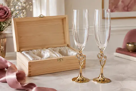 Deux flûtes à champagne en cristal ornées de cœurs, posées près de leur coffret en bois.