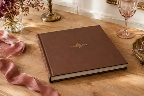 Livre d’or brun à couverture rigide et détail doré, posé sur une table ivoire décorée avec sobriété.